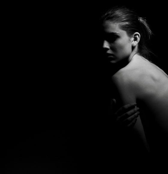 slim and naked woman on black background